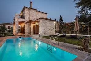 A stone house with a swimming pool, outdoor seating, and a garden.