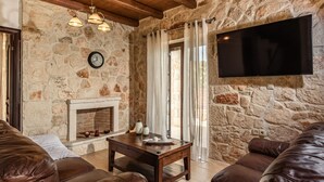 Ein gemütliches Wohnzimmer mit Steinwänden, Kamin, Ledersofas und einem an der Wand befestigten Flachbildfernseher.