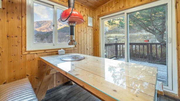 L’intérieur d’une cabane en bois, avec une grande fenêtre, une lampe rouge et une terrasse en bois à l’extérieur.