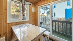 Un intérieur en bois, avec une grande fenêtre, un poêle en métal et une table en bois.