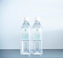 Duas garrafas de plástico transparente com o rótulo "PRINCE SMART INN Água Mineral Natural" e tampa branca, sobre uma superfície refletora contra um fundo neutro.