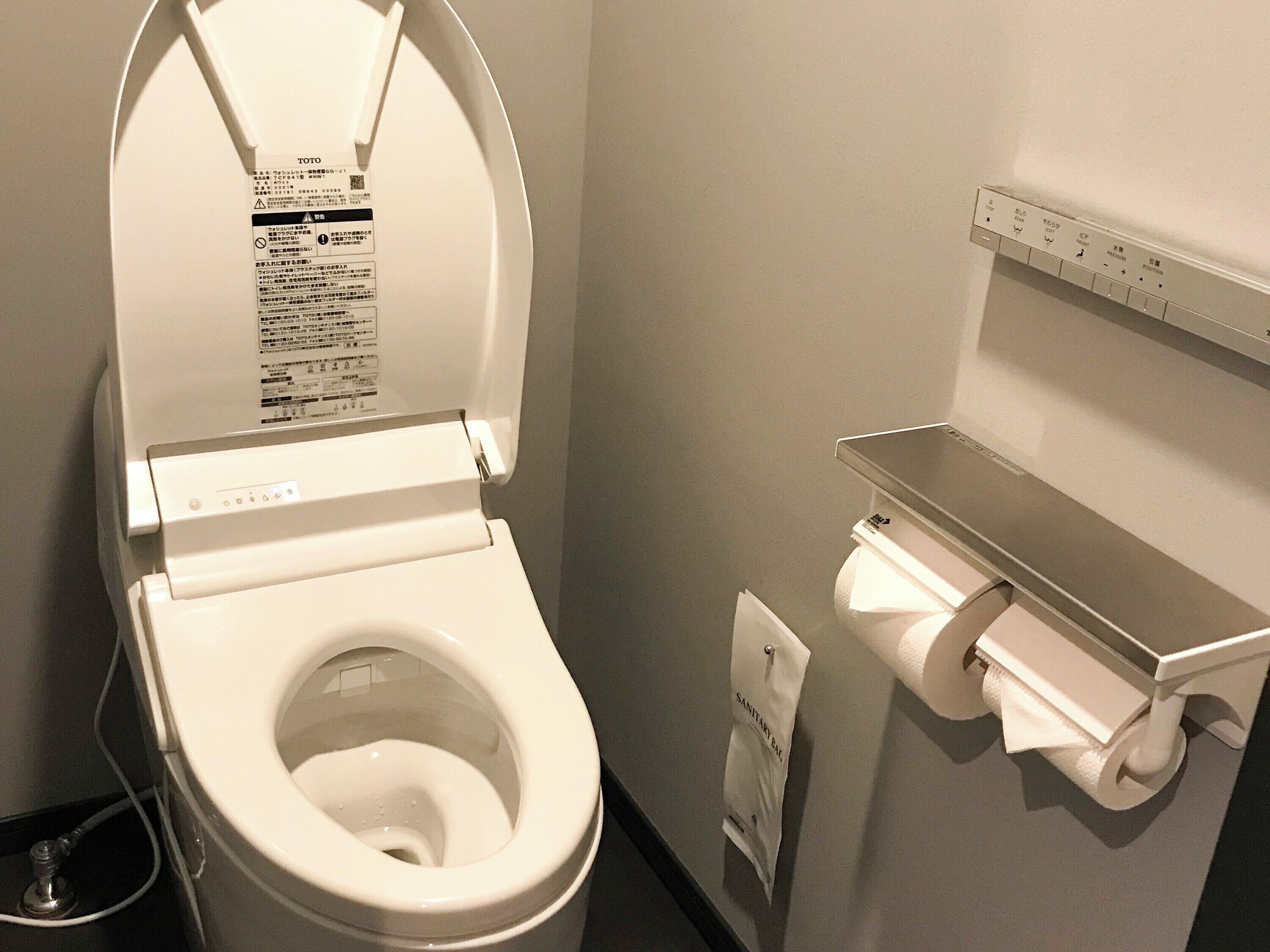 A white toilet with a closed lid, a toilet paper holder, and a small shelf above the toilet.