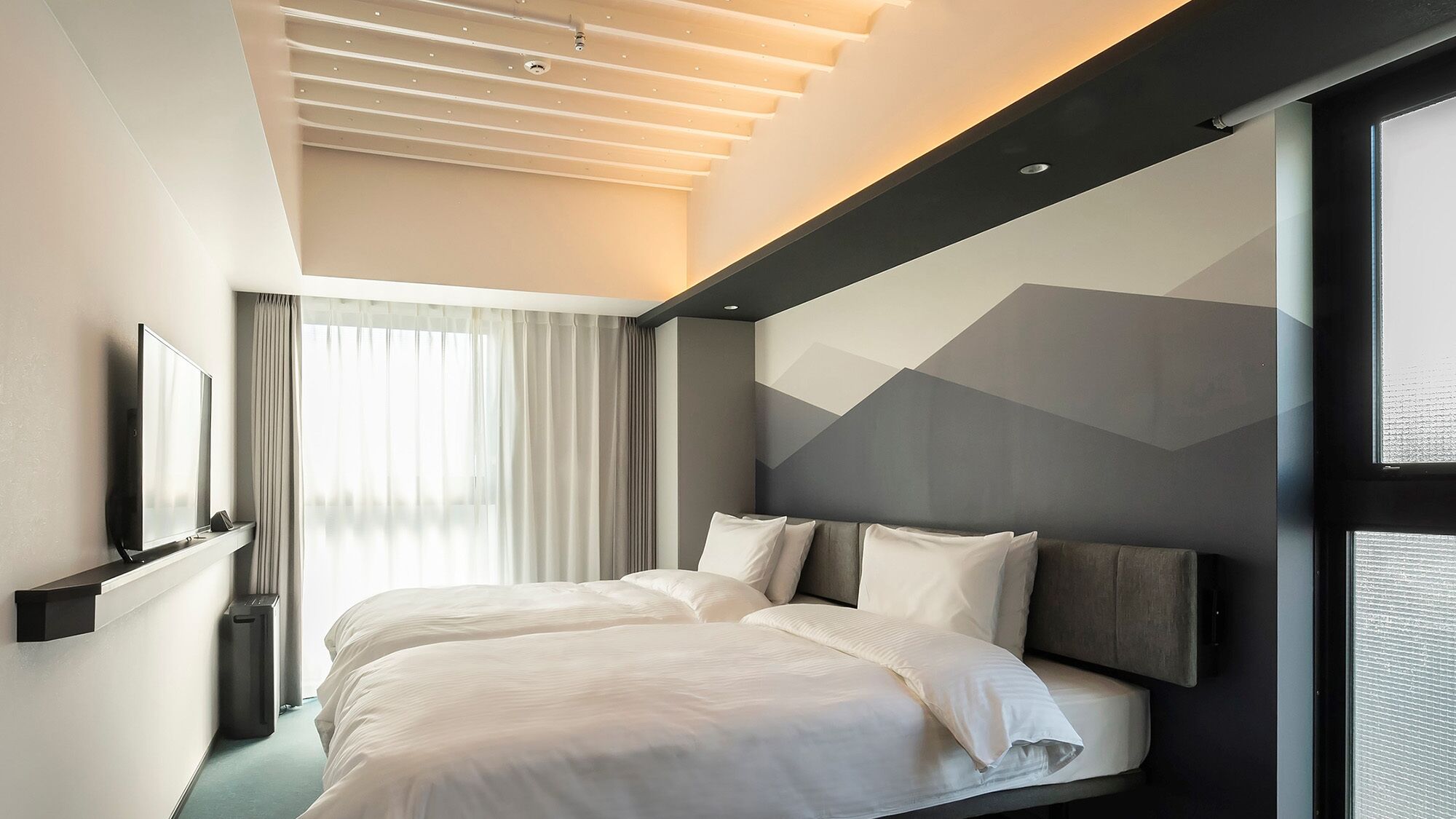 A modern hotel room with a large bed, a TV, and a window with curtains.