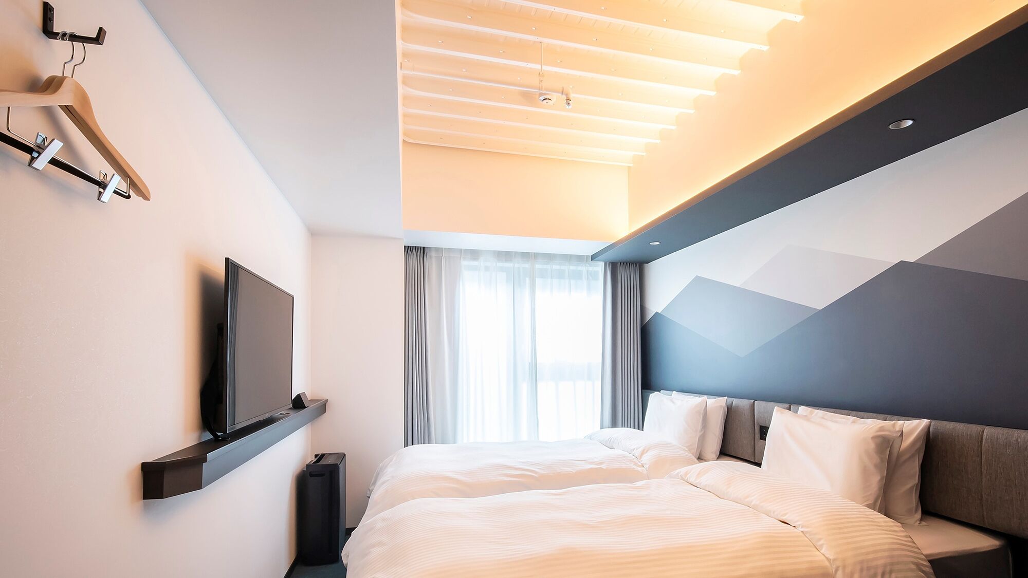A modern hotel room with a bed, a flat-screen TV, a coat rack, and a large window with curtains.