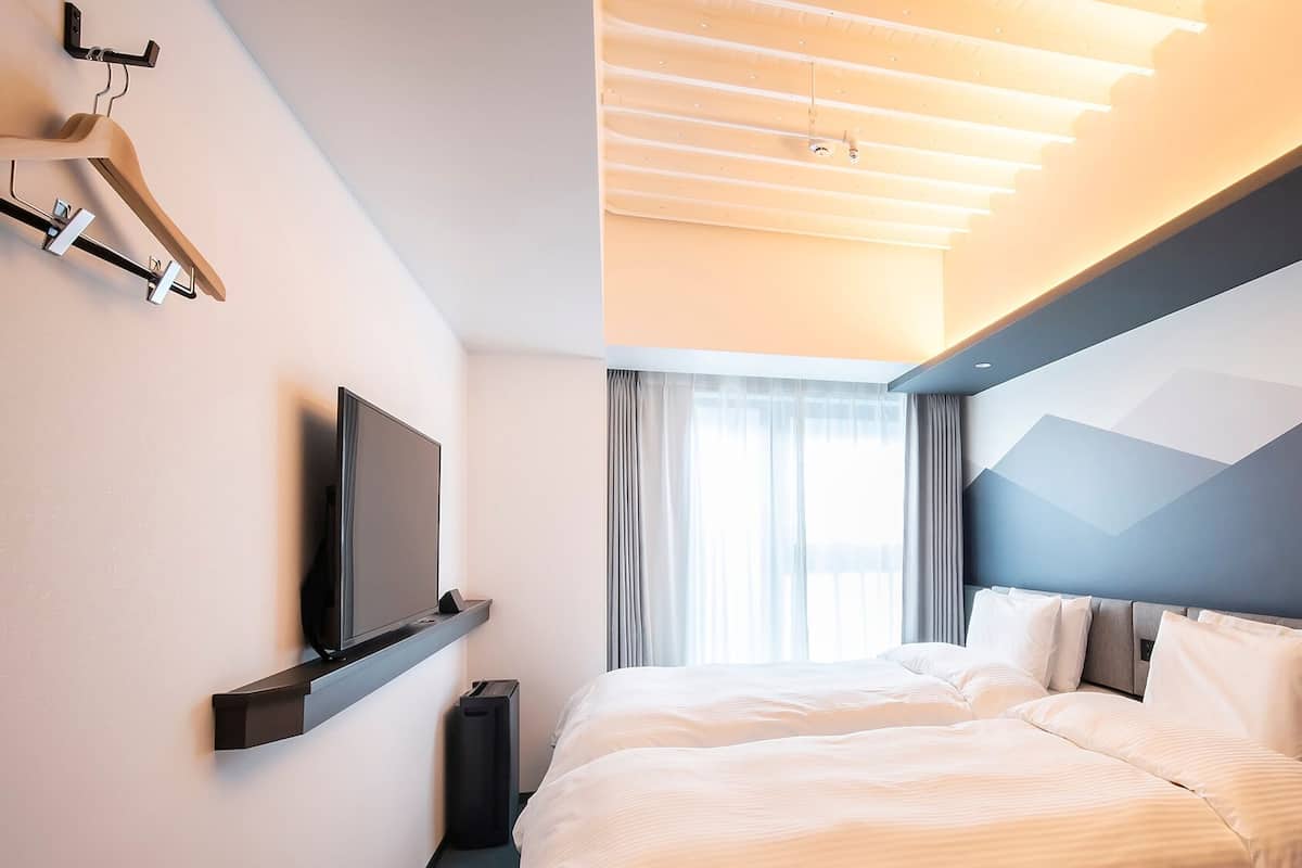 Una habitación de hotel moderna con una cama, un televisor de pantalla plana, un perchero y un ventanal con cortinas.
