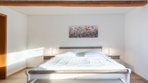A bedroom with a bed, two bedside tables, a nightstand, a painting on the wall, and wooden beams on the ceiling. - Vacation home de Maade for up to 6 people (Enge-Sande)