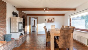 A dining area with a brick fireplace, wooden ceiling beams, and a view through a window. - Vacation home de Maade for up to 6 people (Enge-Sande)