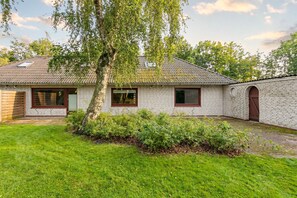 A traditional brick building with a tiled roof, a large tree in the yard, and a well-maintained lawn.