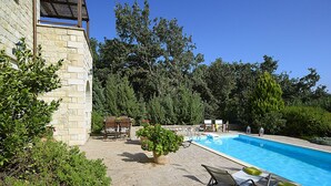 Un edificio de piedra con piscina, mobiliario exterior y vegetación.