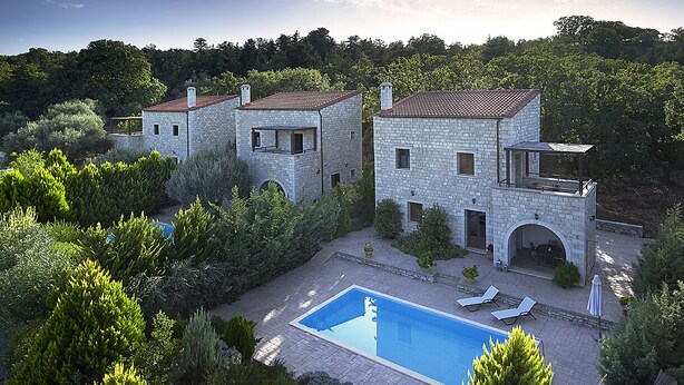 Una villa de piedra con piscina, rodeada de exuberante vegetación.