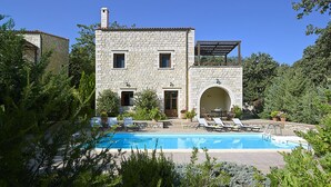 Una villa de piedra con piscina, mobiliario exterior y abundante vegetación.