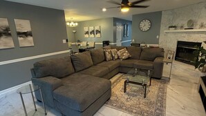 A modern living room with a sectional sofa, a glass coffee table, and a fireplace.