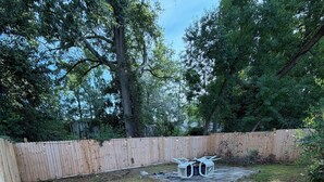 A backyard with a wooden fence, a grassy area, and two white chairs. - Beautifully design house for relaxation (Warner Robins)