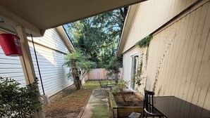 A concrete patio with a table and chairs, surrounded by a wooden fence and greenery.