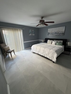 Une chambre à coucher avec un lit, une chaise, un ventilateur de plafond et une fenêtre avec des stores.