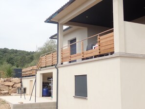 A modern two-story building with a balcony, a water tank, and a stone wall in the background. - A magnificent villa, 5 km from Solenzara. Air conditioning, swimming pool, fenced-in property.   (SOLARO)