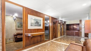 Eine Lobby mit Marmorboden, einer Ledersofa, einem Holztresen, einem gerahmten Bild und einem Spiegel, der das Innere reflektiert.