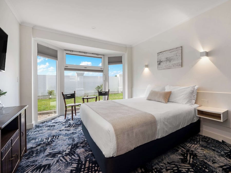 Ein Schlafzimmer mit einem großen Bett, einem Schreibtisch und einem Stuhl in der Nähe einer Glastür, die auf einen Balkon führt.