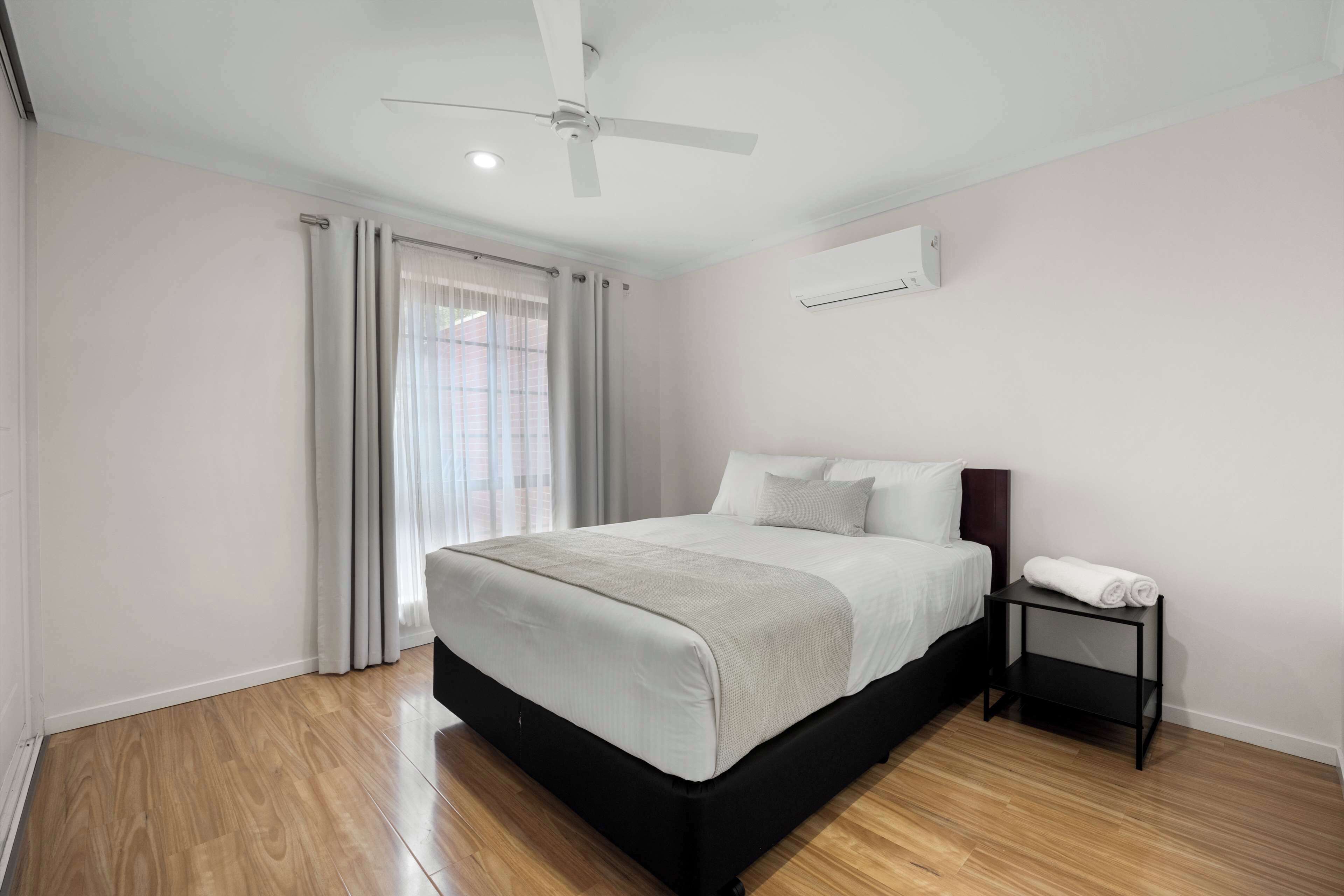 A bedroom with a bed, a ceiling fan, a nightstand, and a window with curtains.