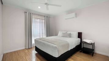 A bedroom with a bed, a ceiling fan, a nightstand, and a window with curtains.