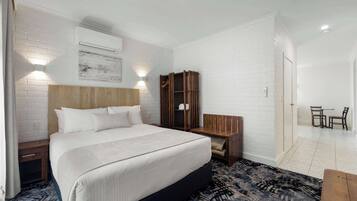Habitación de hotel con una cama grande, una mesita de noche de madera, un armario y una pequeña mesa con sillas.
