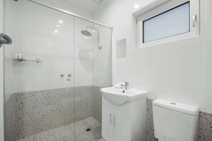 A modern bathroom with a glass shower enclosure, a white sink, and a toilet.