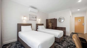 Una camera d'albergo con due letti, una scrivania, una sedia, uno specchio e una porta.