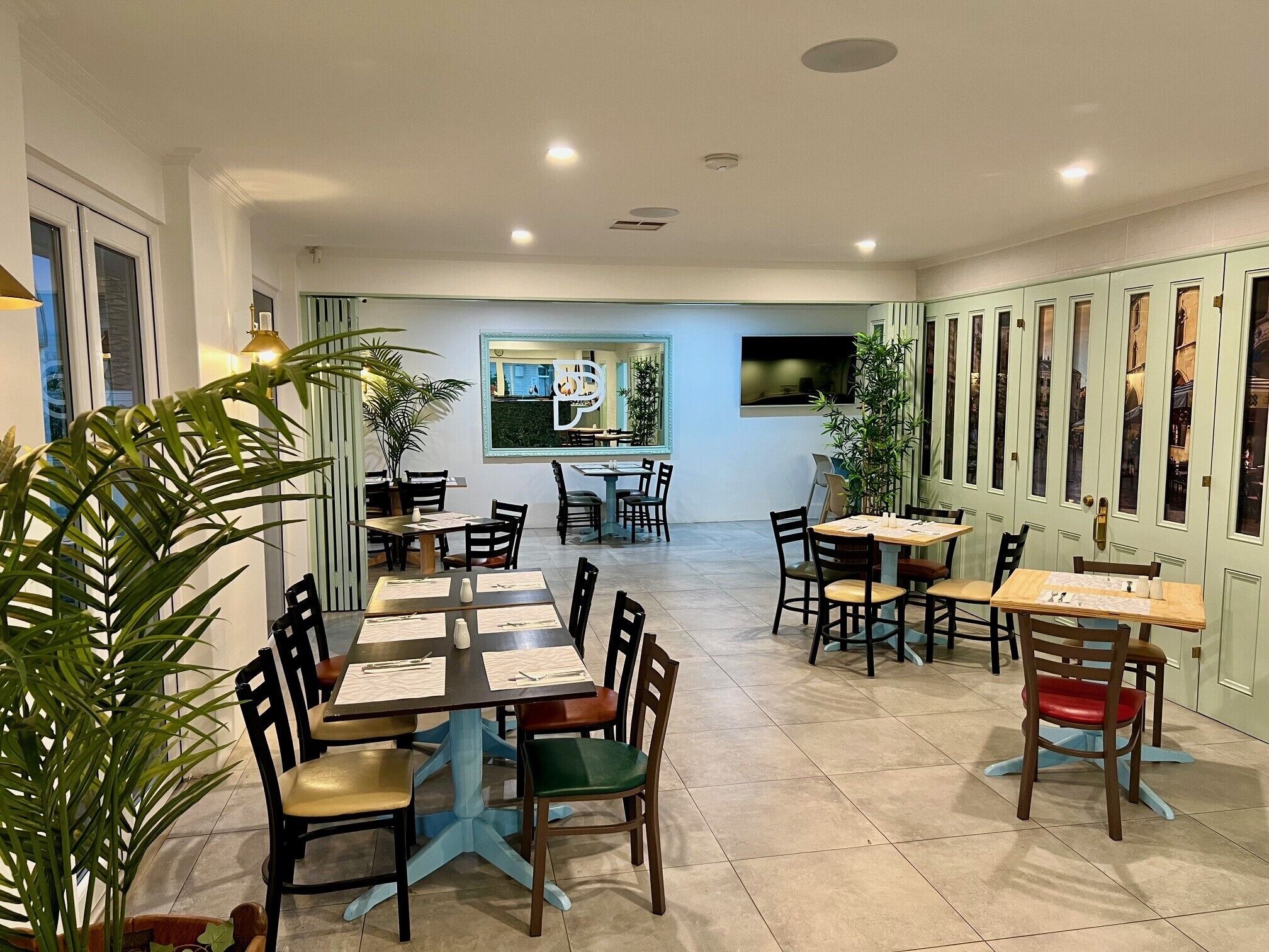 A dining area with multiple tables and chairs, potted plants, and a large window with a view.