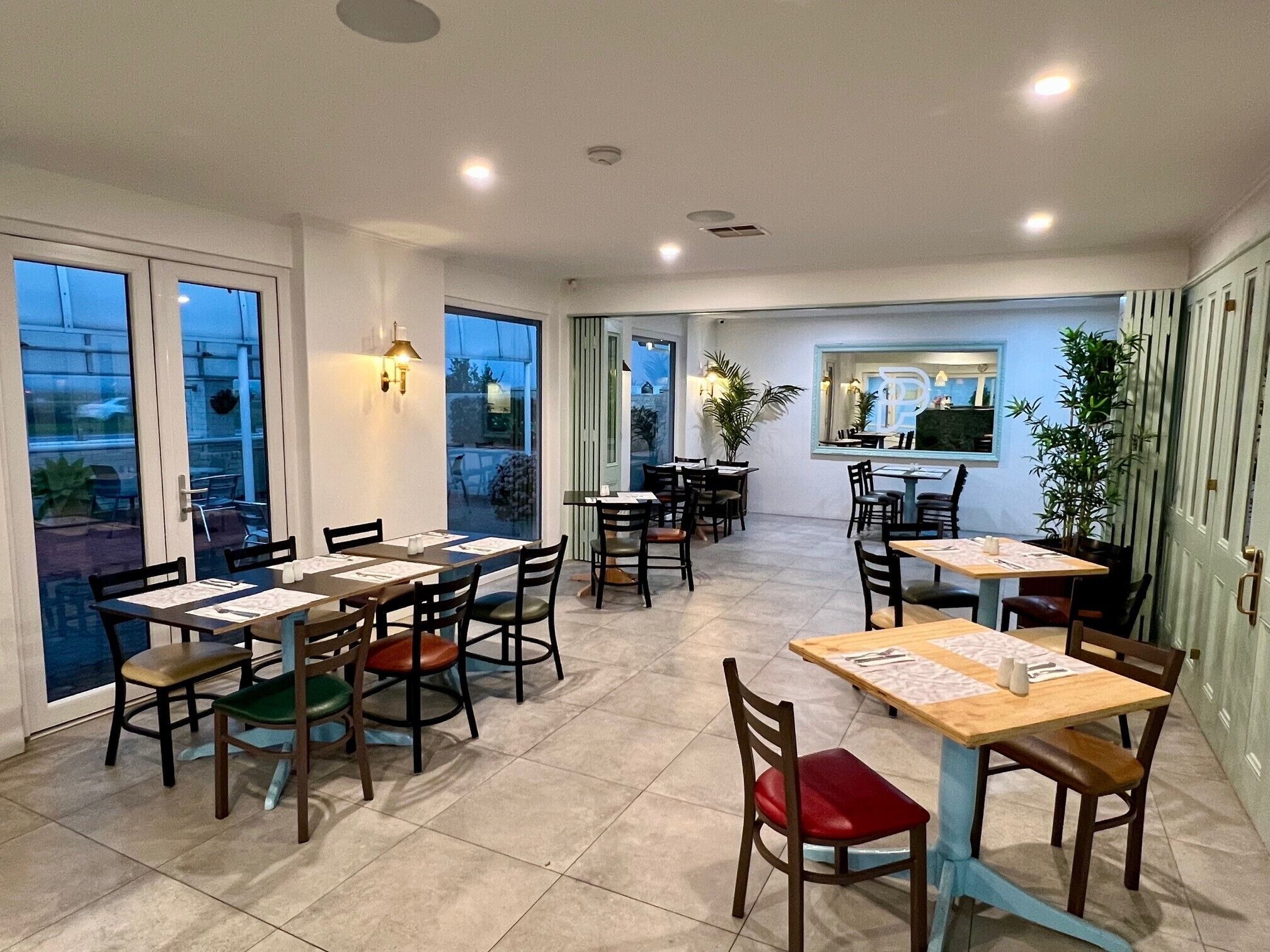 Un restaurant doté de nombreuses tables et chaises, de grandes fenêtres et d’un éclairage intérieur.