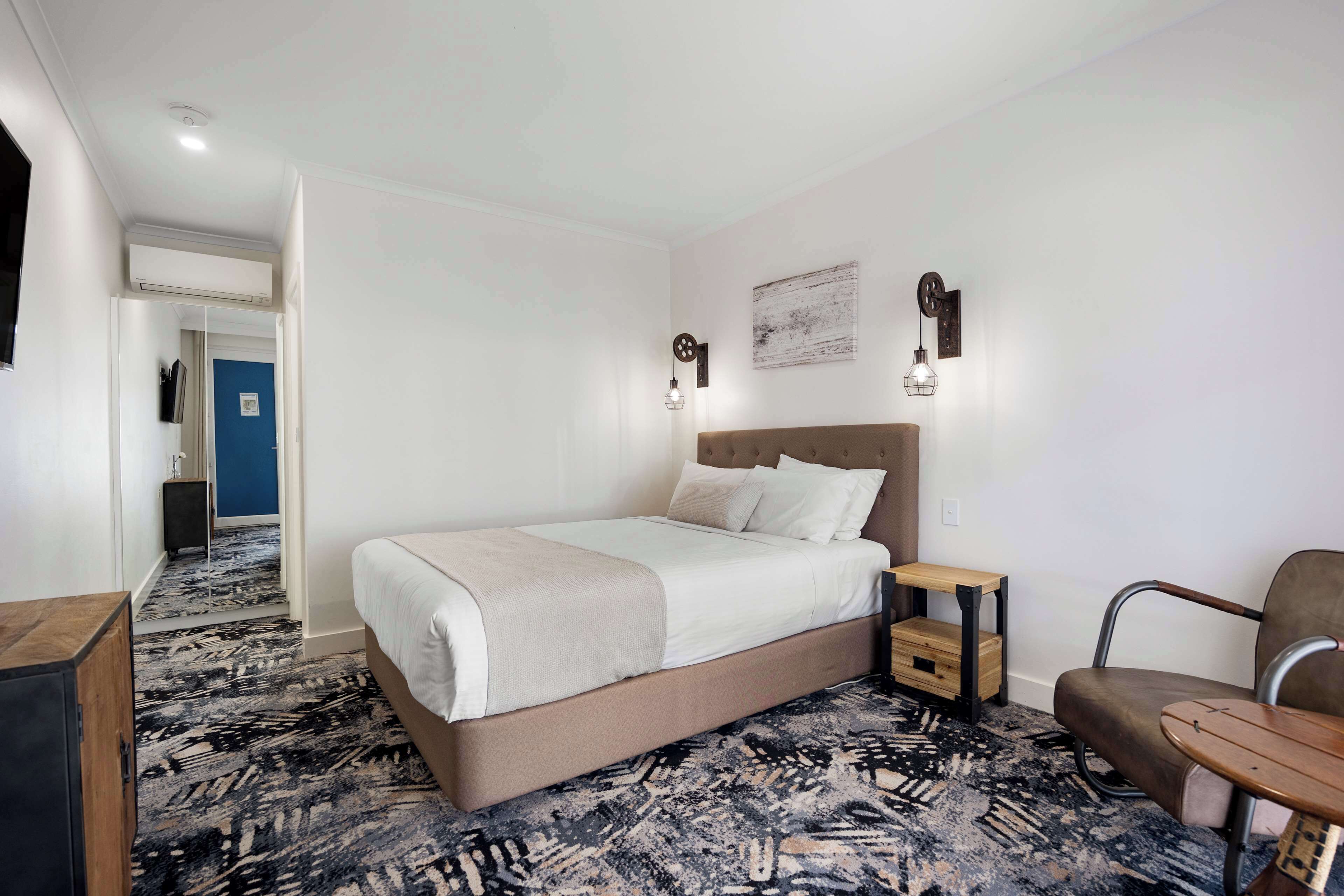 Habitación de hotel con una cama grande, una mesita de noche pequeña, una silla y piso alfombrado.