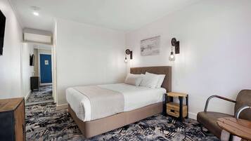 Habitación de hotel con una cama grande, una mesita de noche pequeña, una silla y piso alfombrado.