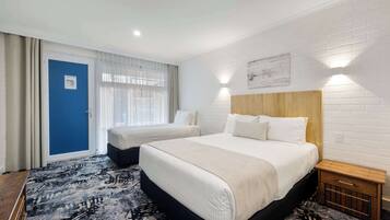 A hotel room with two beds, a blue door, a white brick wall, and a patterned rug.