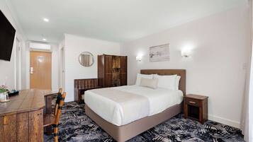 A hotel room with a large bed, a wooden desk, a chair, a wardrobe, and a round mirror on the wall.