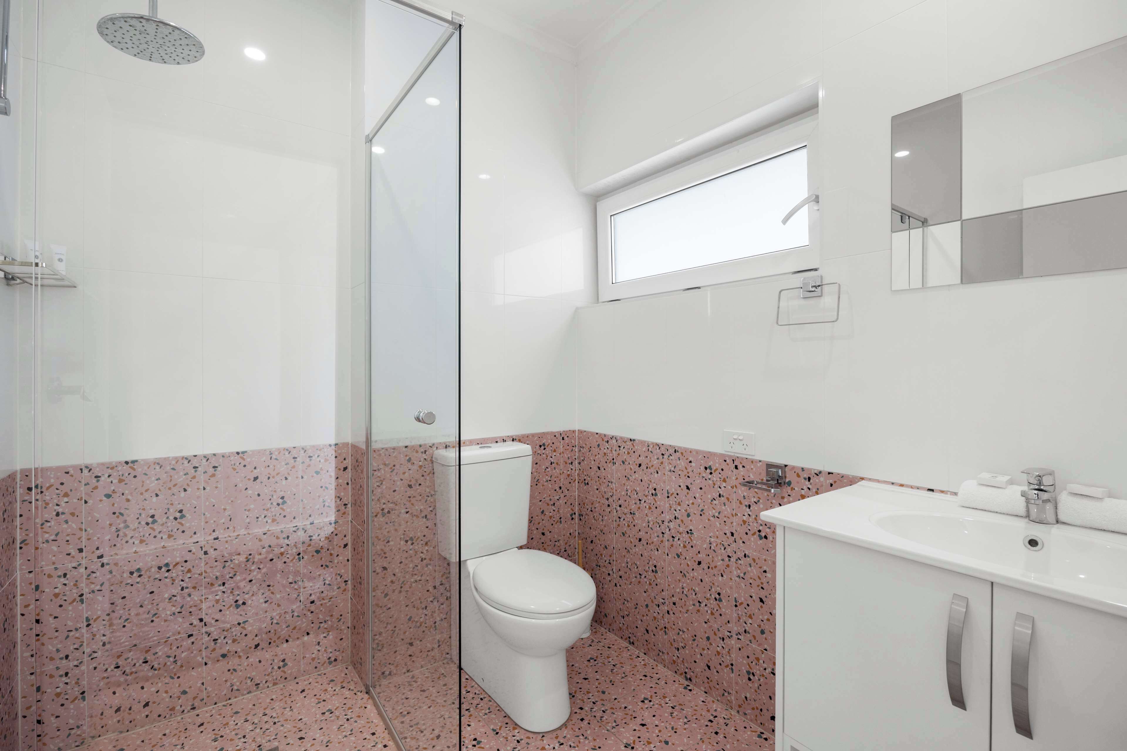 A modern bathroom with a glass shower enclosure, a white toilet, and a vanity with a mirror.