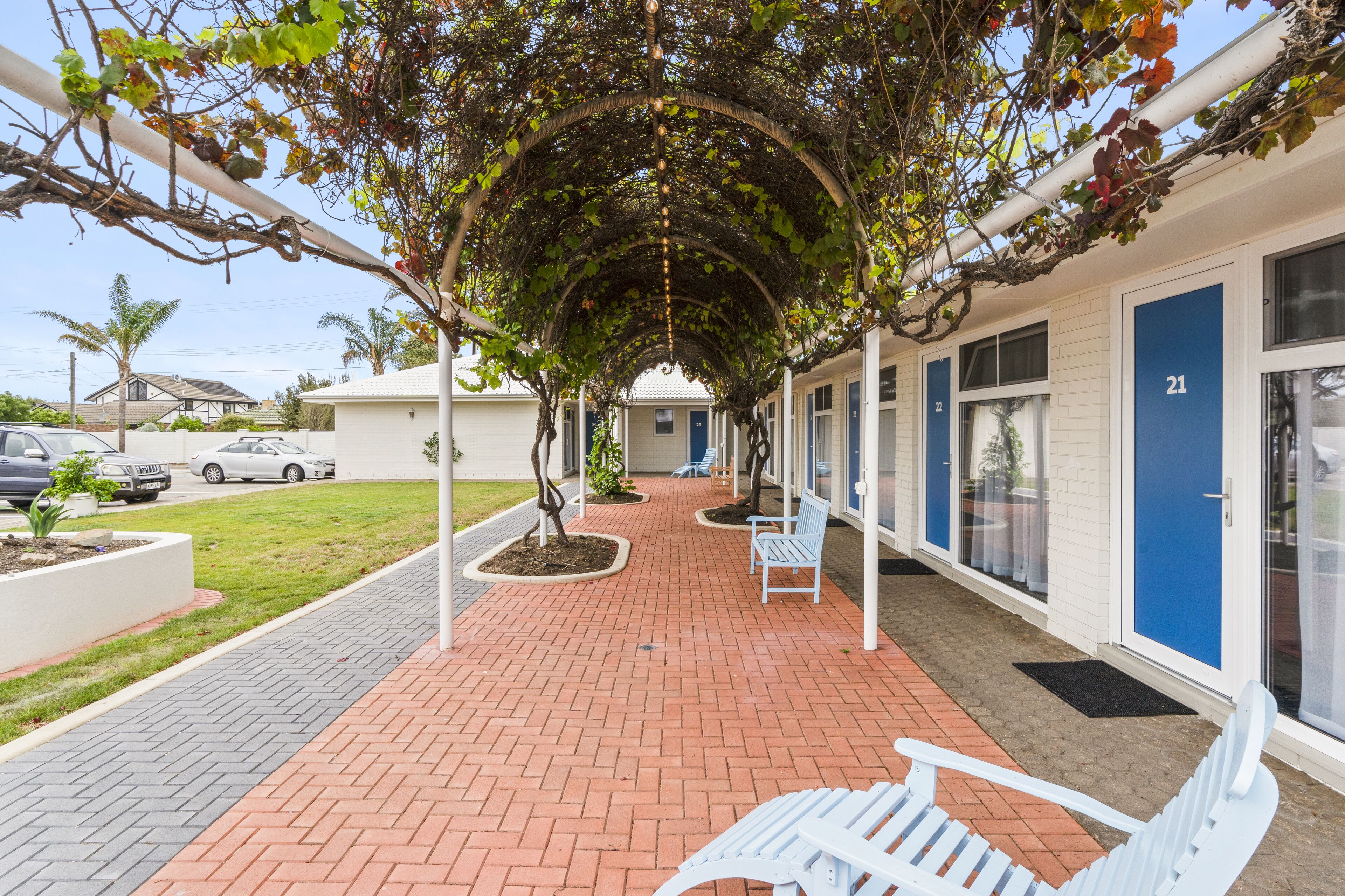 A covered walkway with benches, a brick pathway, and a building with blue doors.