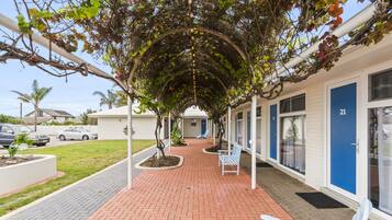 A covered walkway with benches, a brick pathway, and a building with blue doors.