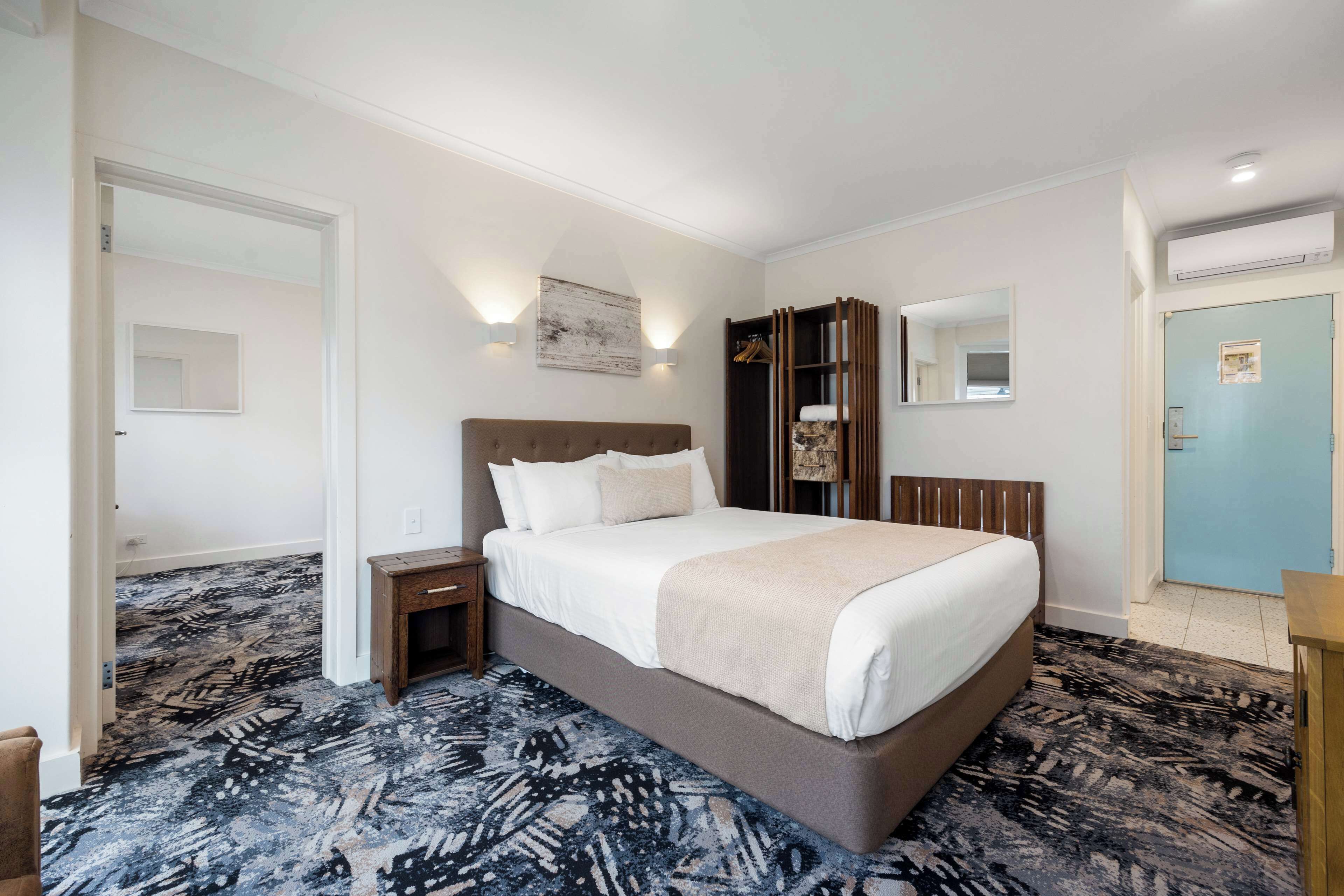 A hotel room with a large bed, a nightstand, a wardrobe, a mirror, and a door.