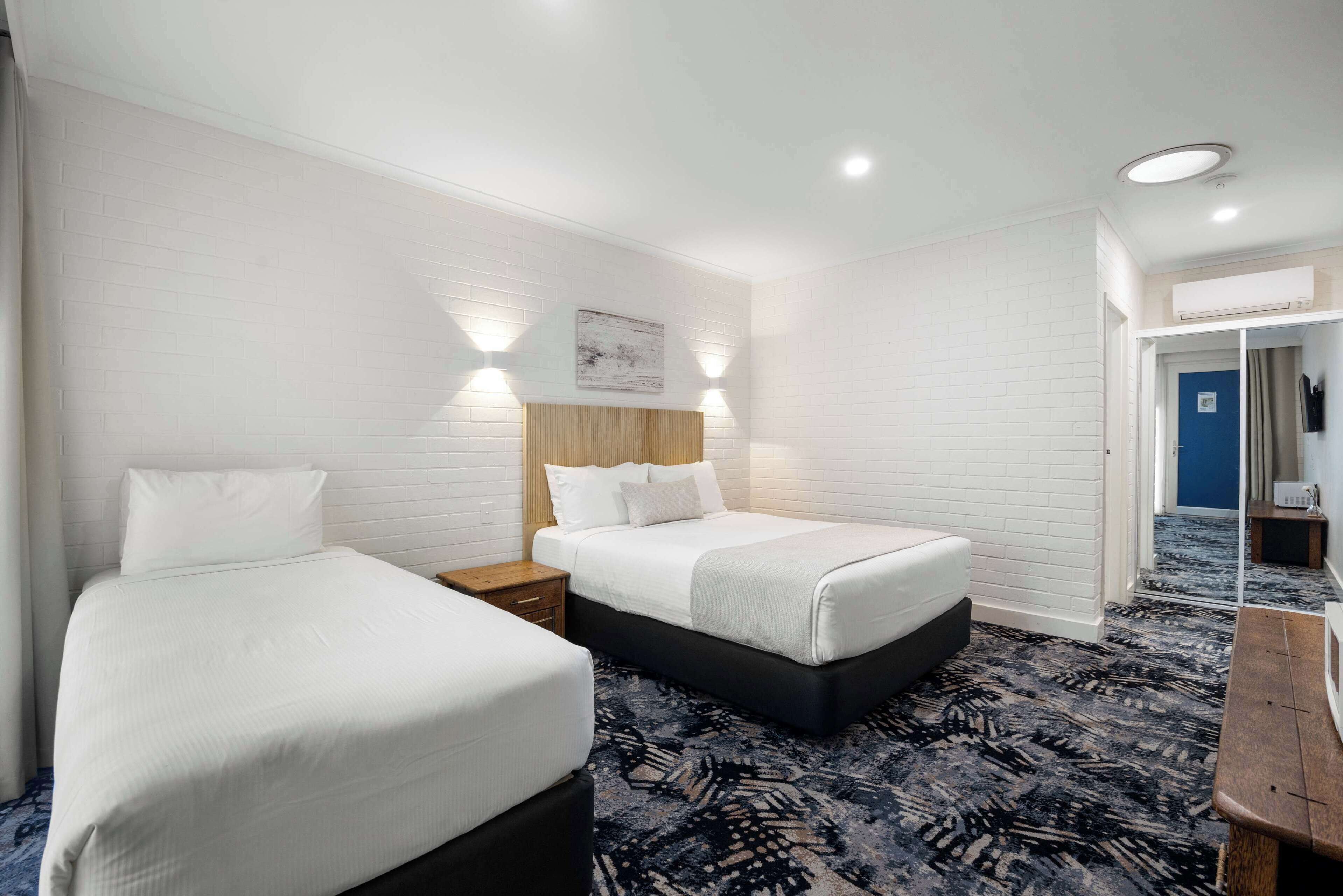 Une chambre d’hôtel avec deux lits, une tête de lit en bois, une moquette à motifs et une porte bleue.