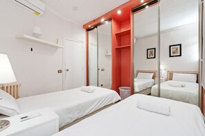 Une chambre d’hôtel avec deux lits, un miroir, une petite table avec une lampe, une étagère avec une lampe et un mur rouge.
