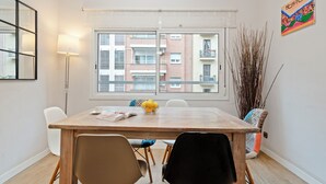 Un comedor con una mesa de madera, cuatro sillas, una lámpara y un ventanal con vistas a edificios.