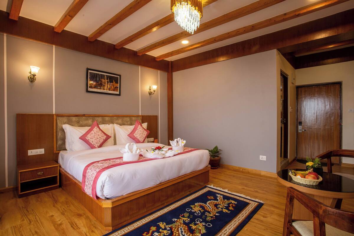A neatly arranged bedroom with a large bed, bedside tables, a small table with fruit, and a chair.