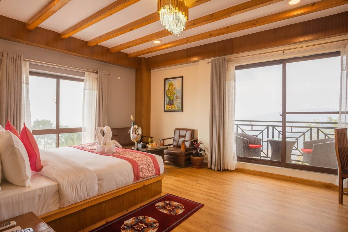 A hotel room with a bed, a desk, a chair, a balcony with outdoor furniture, and a large window.