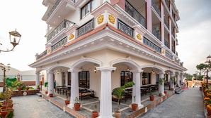 A multi-story hotel with a covered outdoor patio area featuring tables and chairs, potted plants, and a brick pathway.