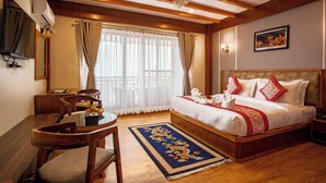 A hotel room with a wooden bed, a dining table with chairs, a TV, and a chandelier.