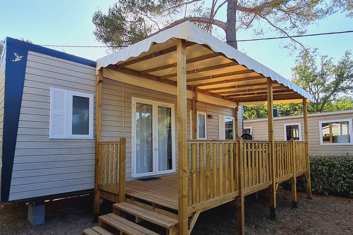 Une terrasse en bois avec un porche couvert, une porte-fenêtre coulissante et un petit espace extérieur aménagé pour s’asseoir.