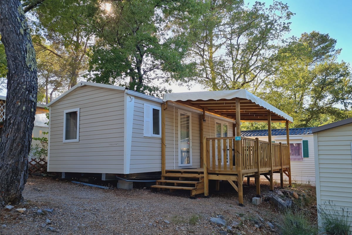 Une petite maison mobile d’un seul étage, dotée d’un porche couvert et d’une petite terrasse.