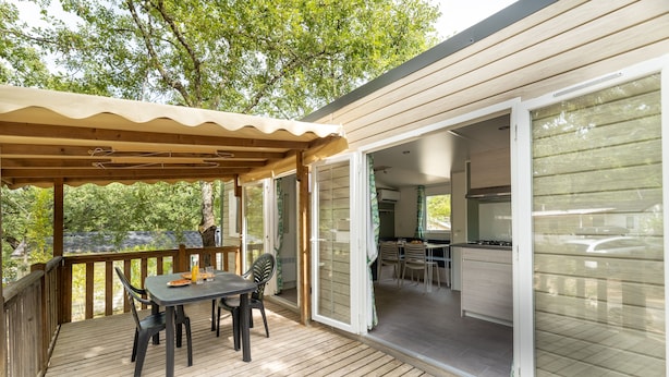 Una terraza techada al aire libre con una mesa y sillas, puertas correderas de vidrio que dan a una zona de cocina.
