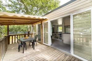Une terrasse extérieure couverte, dotée d’une table et de chaises, et de portes-fenêtres coulissantes donnant sur un espace cuisine.