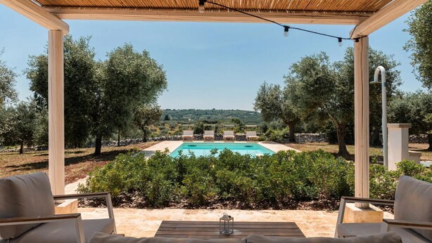 Zona d'estar a l'aire lliure coberta amb piscina i oliveres al fons.