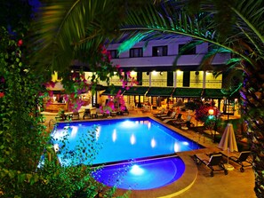 A pool area with lounge chairs and umbrellas, surrounded by greenery and a building with multiple windows. - Hotel Bleu Nuit Bodrum (Bodrum)
